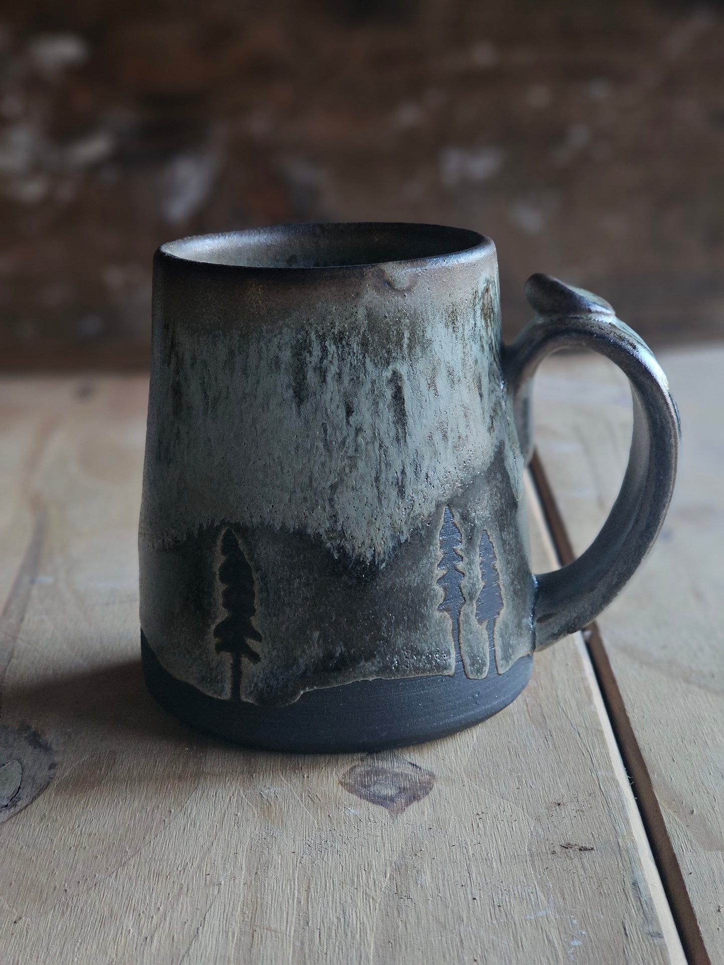 Handmade stoneware mug with carved pine tree silhouettes - green glaze flowing into dark gray - artisan pottery